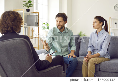 Young couple sitting on sofa and talking with psychologist on therapy session. Young couple sitting on sofa and talking with psychologist on therapy session. 127900432