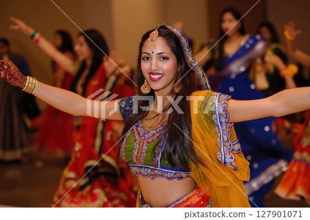 Indian woman wearing traditional dress is smiling while performing a dance on stage with other people 127901071