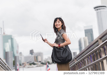 Happy young southeast asian woman teenager blogger using smartphone searching travel guide. World travel explorer tourism concept local cultural experience in Bangkok Asia near Chao Phraya river 127901389