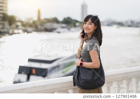 Happy southeast asian teenager solo world travel explorer blogger on tourism trip in Asia. local cultural experience in Bangkok Thailand wait for an express boat on Chao Phraya river Happy southeast asian teenager solo world travel explorer blogger on tourism trip in Asia. local cultural experience in Bangkok Thailand wait for an express boat on Chao Phraya river 127901406