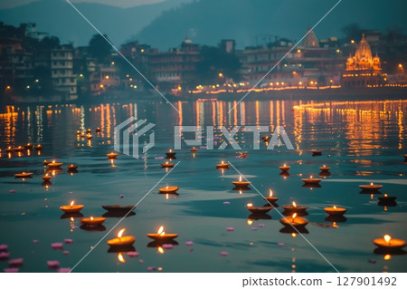 Floating diya lamps illuminating a river at twilight, with a city skyline in the background 127901492