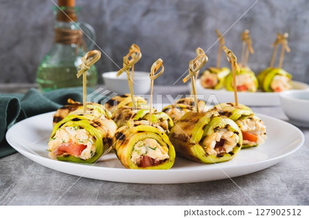 Zucchini appetizer rolls with ricotta, tomato and garlic filling on a plate on a table 127902512