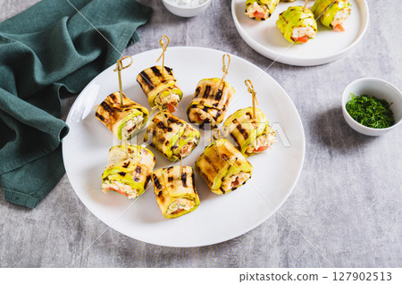 Grilled zucchini rolls filled with cream cheese and tomatoes on a plate on the table 127902513