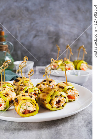 Zucchini appetizer rolls with ricotta, tomato and garlic filling on a plate on a table vertical view 127902514