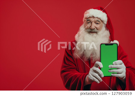 Santa claus holding smartphone with green chroma key screen on red background 127903059