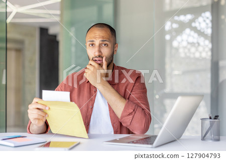 Portrait of upset worried man inside office, employee received letter with bad and sad news in mail. Businessman holding envelope with notification and looking at camera. Portrait of upset worried man inside office, employee received letter with bad and sad news in mail. Businessman holding envelope with notification and looking at camera. 127904793
