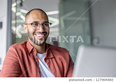 A happy, smiling man with glasses looking to the side, wearing a red shirt, with soft lighting. A happy, smiling man with glasses looking to the side, wearing a red shirt, with soft lighting. 127904860