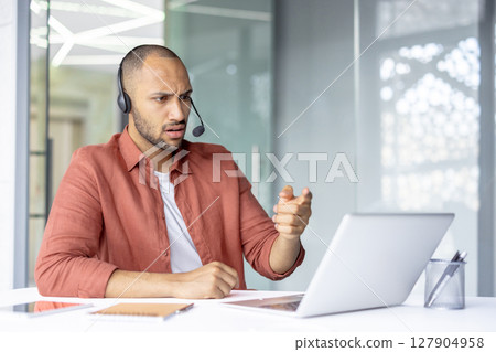 A man with a headset gestures emphatically during a video call, expressing surprise and consternation with his facial expression. 127904958