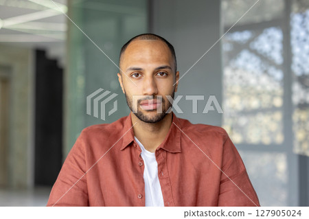 A portrait of a young man with a short haircut and a red shirt, looking directly at the camera. 127905024