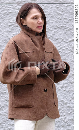 A middle-aged woman in a warm coat shielding herself from the cold. This moment reflects warmth and stress associated with life changes like menopause. 127906201
