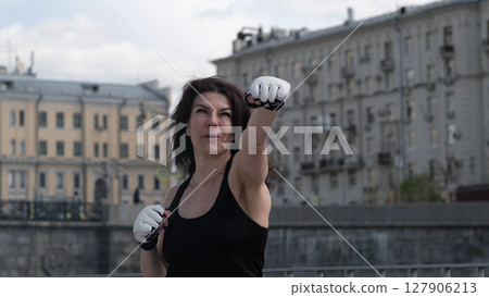 A determined woman throws a punch in an outdoor boxing workout, exuding strength and intensity. This image represents resilience, self-defense, and personal empowerment. 127906213