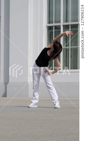 A woman performs a side stretch outdoors, focusing on flexibility and body balance. This image represents wellness, mobility, and an active lifestyle. 127906214