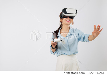 VR game fun as Young Asian woman smiles while playing VR game using joystick controller and touching virtual panel with palm in immersive reality. isolated studio white background 127906261