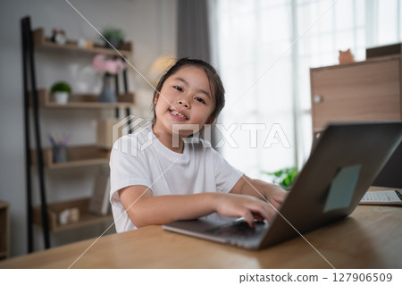 Cheerful young girl engaging in online learning while using laptop in cozy home office, showcasing modern educational environment and technology use Cheerful young girl engaging in online learning while using laptop in cozy home office, showcasing modern educational environment and technology use 127906509