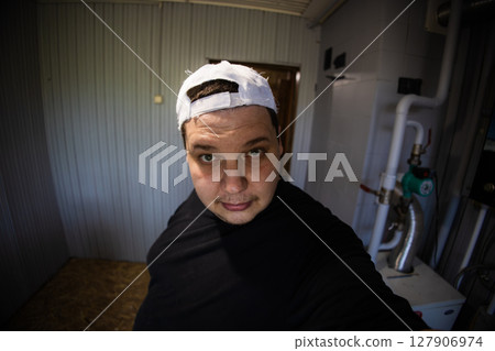 Technician wearing a white cap inspecting a heating system in a boiler room, ensuring optimal operation and thorough maintenance for safety and energy efficiency. Technician wearing a white cap inspecting a heating system in a boiler room, ensuring optimal operation and thorough maintenance for safety and energy efficiency. 127906974