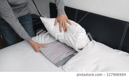 man puts his pajamas under his pillow 127906984