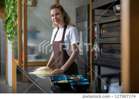 Young woman in apron kneading the dough for cooking pizza 127907174