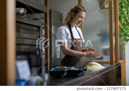 Young woman in apron kneading the dough for cooking pizza Young woman in apron kneading the dough for cooking pizza 127907175