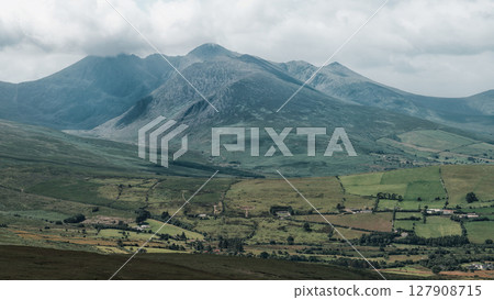 Mountain under cloudy skies with a valley in Ireland, showing vast green grass. Mountain under cloudy skies with a valley in Ireland, showing vast green grass. 127908715