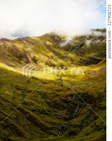 Viewing dramatic green landscape and sparse waterfalls on Carrauntoohil mountain walkway in County Kerry, Ireland, during a cloudy day. 127908723