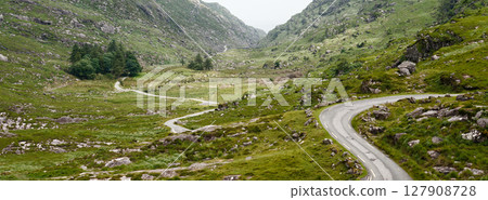 Emerald hillsides embrace a narrow asphalt road, creating a mesmerizing journey through Ireland's heart. Emerald hillsides embrace a narrow asphalt road, creating a mesmerizing journey through Ireland's heart. 127908728