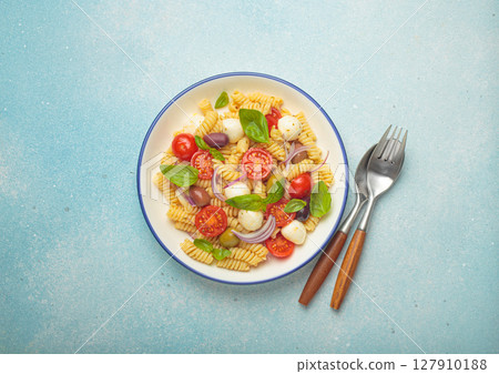 Italian pasta salad with fusilli, cherry tomatoes, mozzarella, olives, basil on blue background top view, Italian cuisine Italian pasta salad with fusilli, cherry tomatoes, mozzarella, olives, basil on blue background top view, Italian cuisine 127910188
