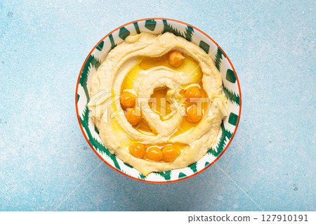 Bowl of hummus garnished with chickpeas and olive oil in bowl on blue background top view 127910191