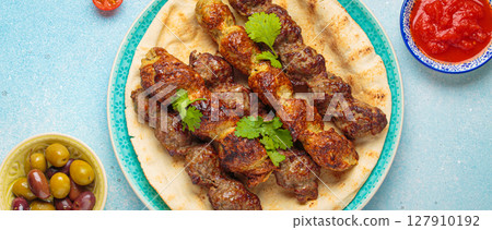 Kofta meat kebabs with pita bread, tomato sauce, and coriander on blue plate top view on light beige background 127910192