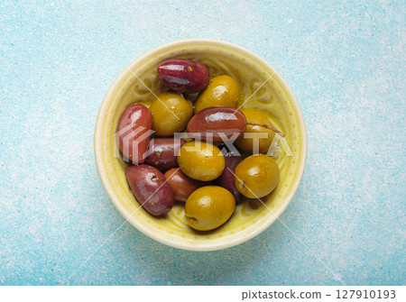 Green and black olives resting in ceramic bowl on blue background top view Green and black olives resting in ceramic bowl on blue background top view 127910193