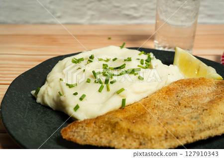 Breaded fish fillet with mashed potatoes and chives on black plate 127910343