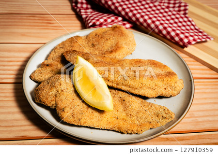Breaded chicken breast fillets with lemon slice on wooden table Breaded chicken breast fillets with lemon slice on wooden table 127910359