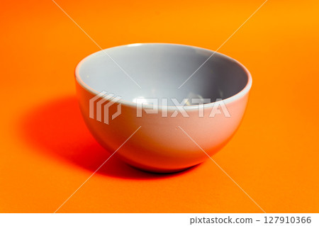 Empty gray bowl sitting on vibrant orange background casting shadow 127910366