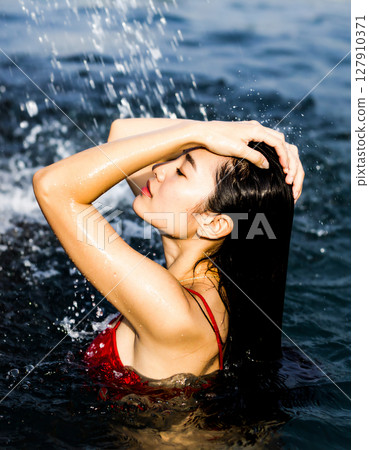 一名身穿比基尼泳裝的女子在海裡嬉戲玩耍的照片 一名身穿比基尼泳裝的女子在海裡嬉戲玩耍的照片 127910371