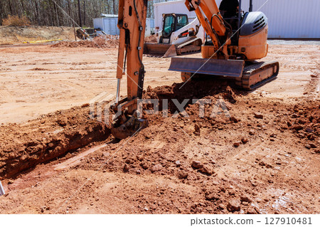 Heavy machinery is digs trench as workers prepare for construction location. Heavy machinery is digs trench as workers prepare for construction location. 127910481