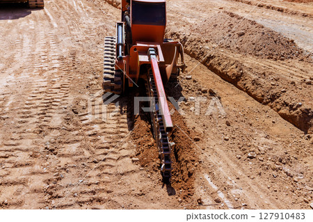 Heavy trenching machinery digs into dry ground, creating trench in construction area Heavy trenching machinery digs into dry ground, creating trench in construction area 127910483