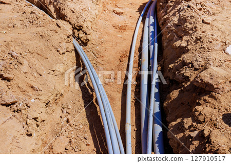 Workers install various electrical pipes in deep trench at construction site 127910517