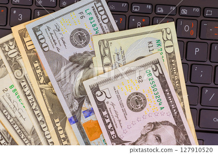 Currency US dollar banknotes of various denominations are placed on black laptop keyboard Currency US dollar banknotes of various denominations are placed on black laptop keyboard 127910520