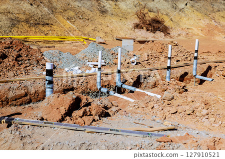 Wastewater plumbing pipes are positioned in freshly excavated area at construction site during work day 127910521