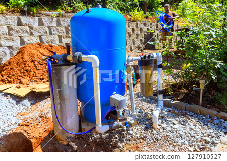Workers set up artesian water well system in garden surrounded by gravel 127910527