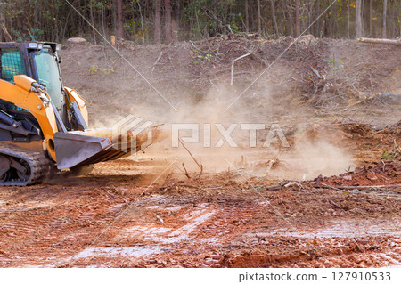 Heavy machinery operates in deforested area, moving soil, debris while dust rises into air. Heavy machinery operates in deforested area, moving soil, debris while dust rises into air. 127910533