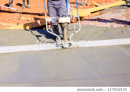Workers are using concrete leveling tool to smooth out freshly poured cement at construction site. 127910535