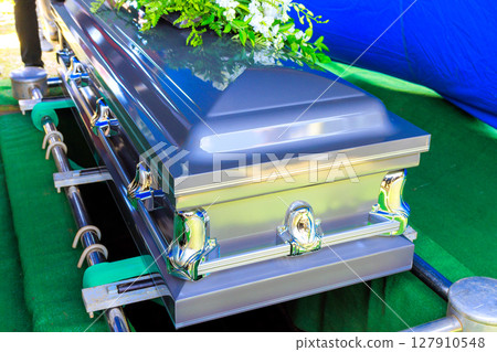 Family, friends gather around flower adorned coffin during solemn burial funeral service in peaceful setting. 127910548