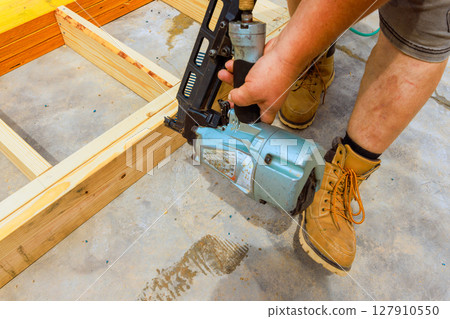 Worker is focused on using nail gun to secure wooden beams to floor in construction zone 127910550