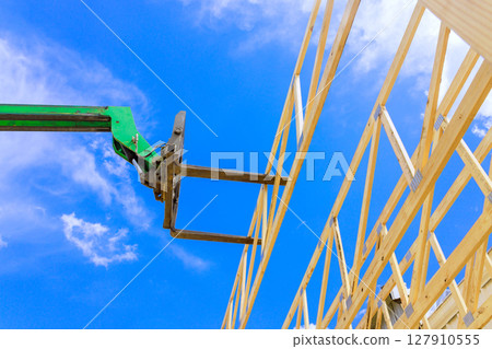 Heavy telehandler machinery lifts wooden beams for construction of new structure on construction area. 127910555
