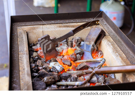 Blacksmiths traditional metalworking techniques using heated tools in axe making setting. 127910557