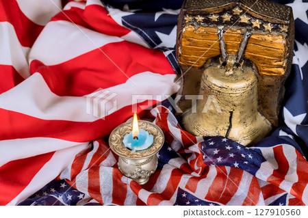 USA bell, candle rest on an American flag, symbolizing liberty remembrance symbol of freedom in reflective moment. USA bell, candle rest on an American flag, symbolizing liberty remembrance symbol of freedom in reflective moment. 127910560