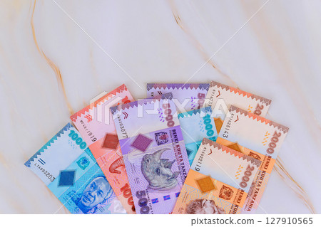 Various Tanzanian shilling banknotes in vibrant colors are spread out on smooth, light colored surface 127910565
