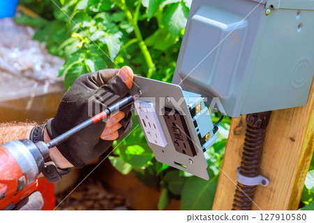 Homeowner works on installing an outdoor electrical outlet in garden during works day 127910580