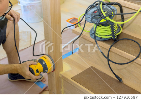 Craftsman uses power sander on wooden railings while during home renovation. 127910587