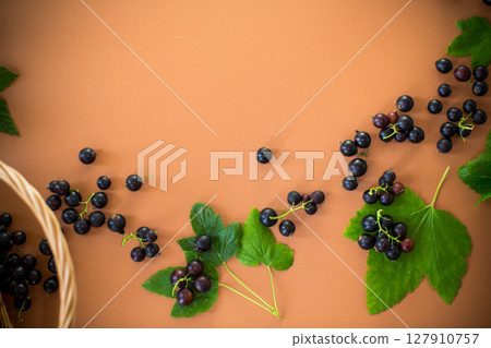 Scattered currant berries next to a basket on a brown background 127910757